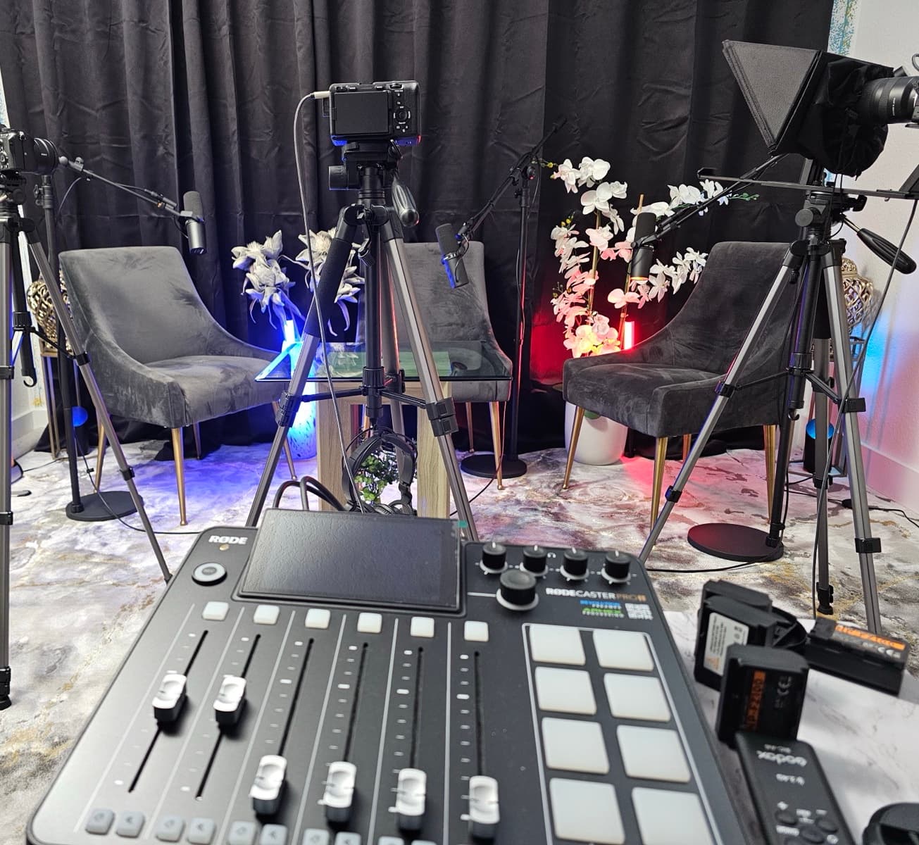 RODECaster Pro II audio mixing console in the foreground, with the cameras and the podcast seating area behind it